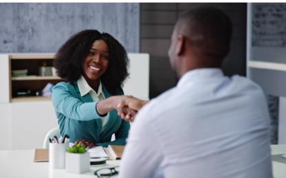 Two people shaking hands seated at a table. 