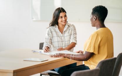 Image of two individuals sitting a table discussing a topic and preparing for an interview.