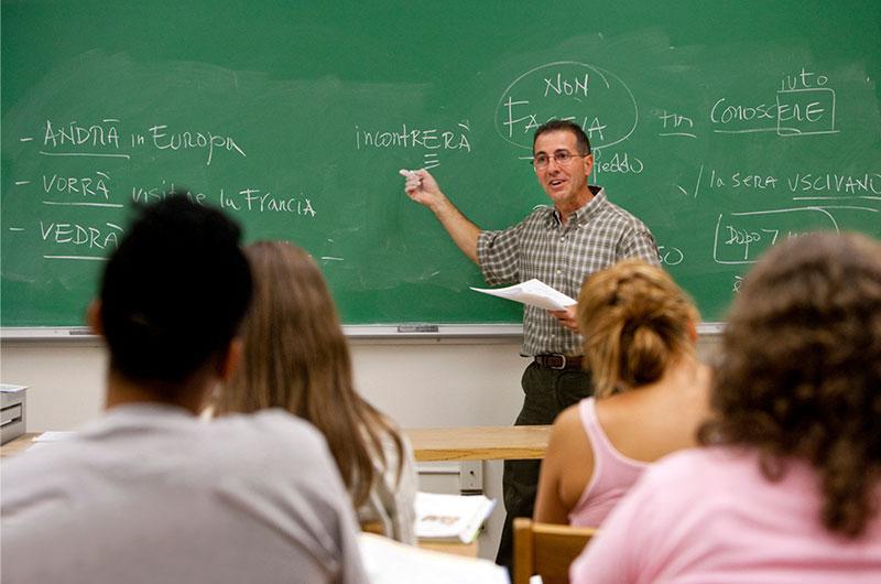 Male professor at the front of class lecturing and using green chalkboard
