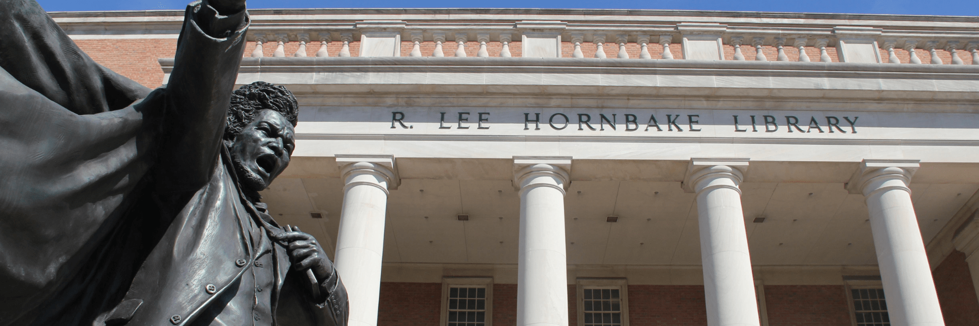 The exterior of Hornbake Library with the Frederick Douglass statue in-frame of the image.