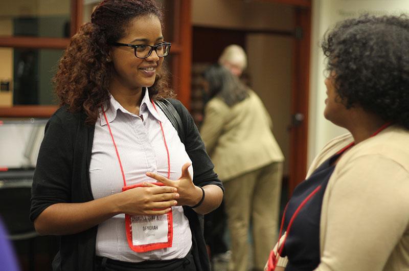 A woman wearing a name tag lanyard speaks with a recruiter during a networking event.