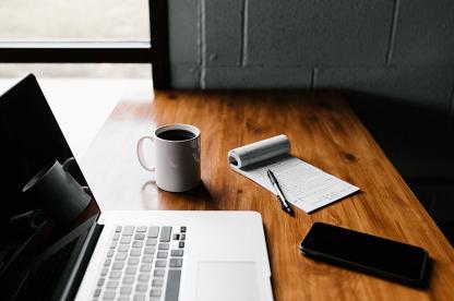 Laptop, coffee mug, and notepad on wooden desk